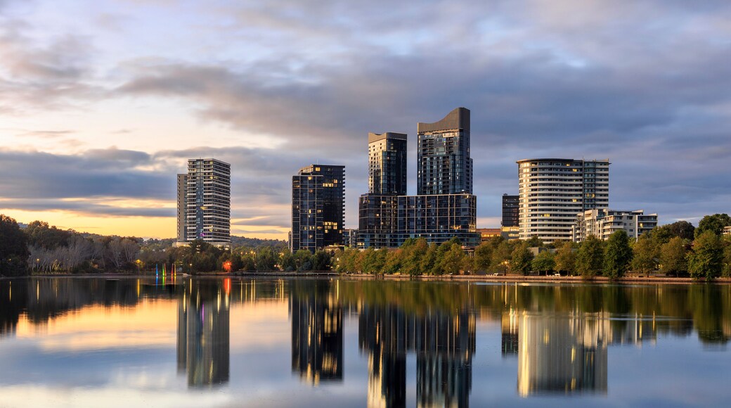 A city skyline reflected in a calm lake with modern high-rise buildings.