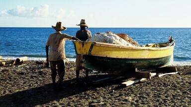 Rear view of two men near a boat on a beach on the island of Martinique, Caribbean