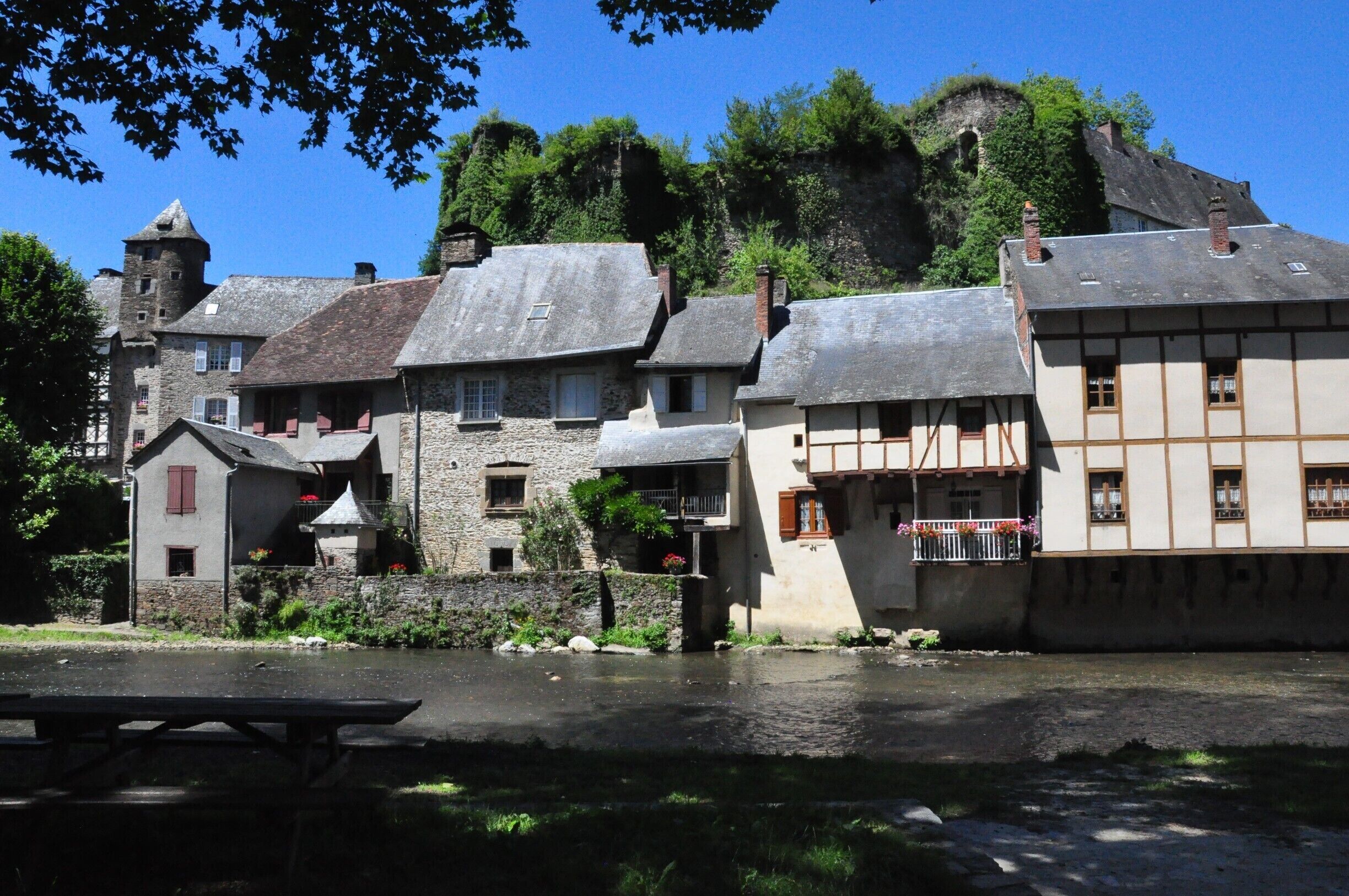 A riverside village with stone buildings, a tower, and lush greenery.