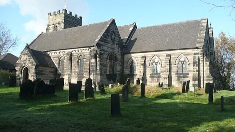 A historic stone church with a tower and arched windows, surrounded by a cemetery.