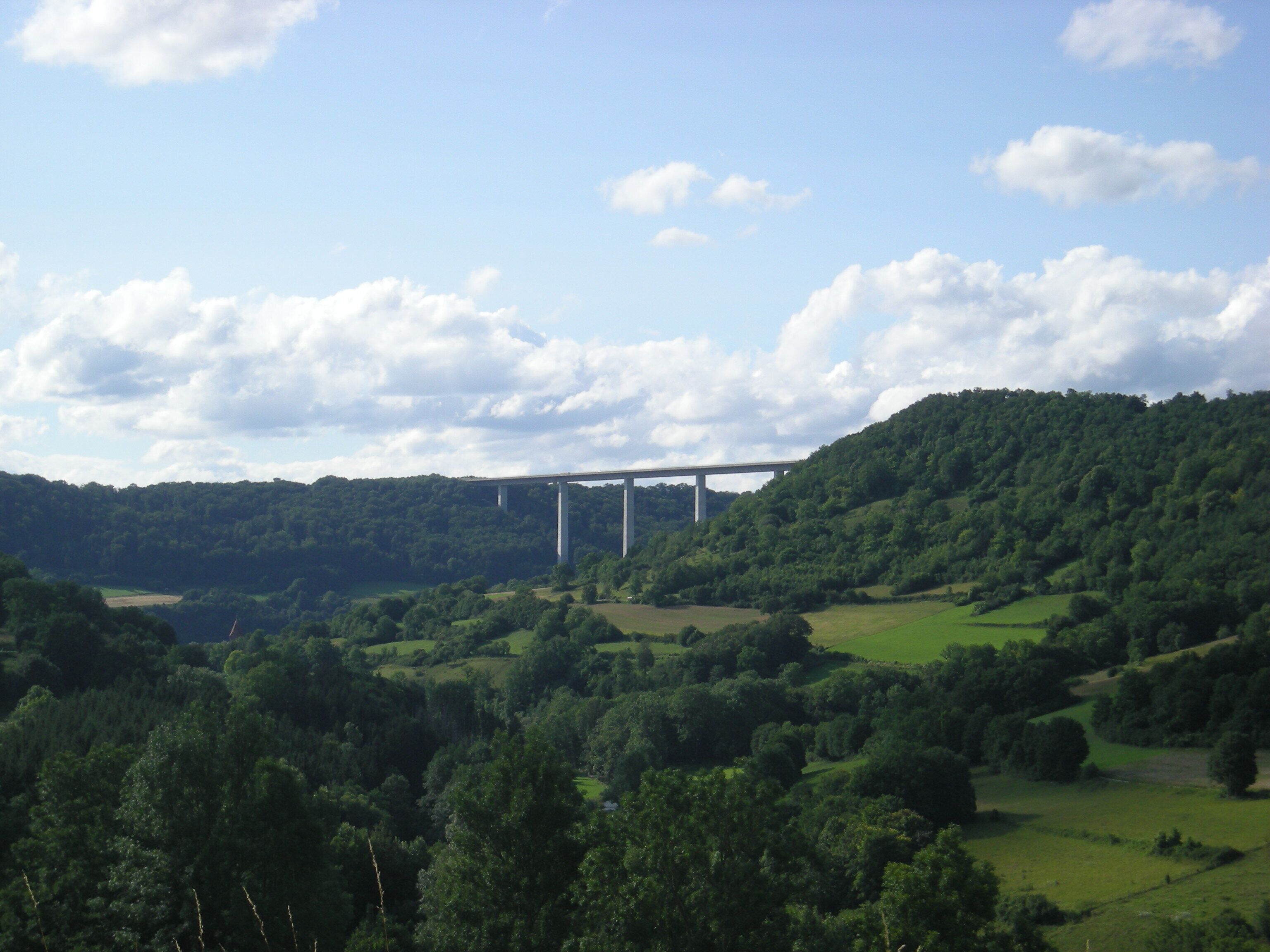 A bridge over a valley with lush green hills and a clear sky.