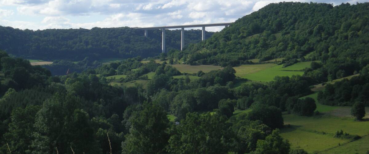 A bridge over a valley with lush green hills and a clear sky.