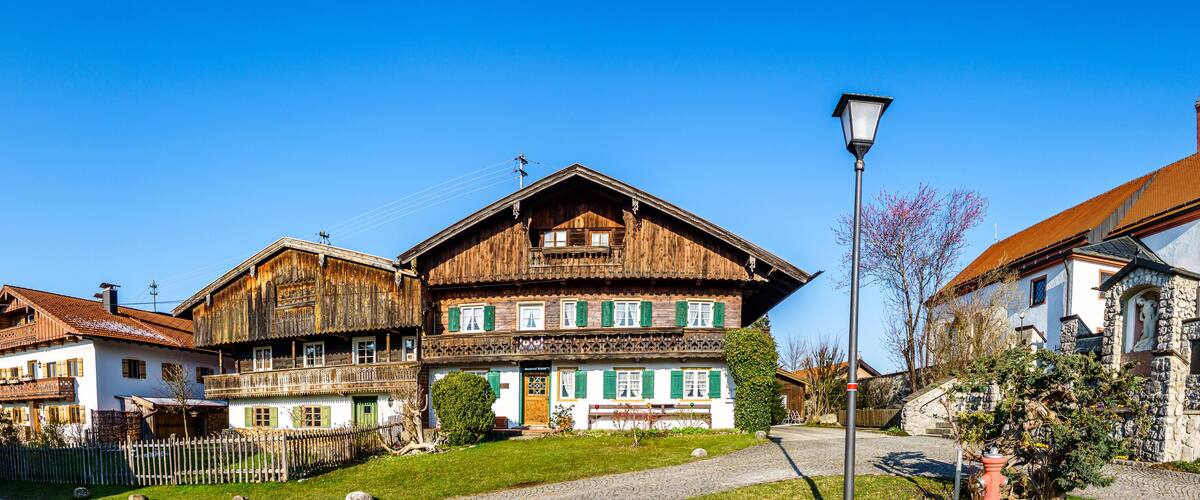 A traditional wooden house with a balcony, a church with a clock tower, and a clear blue sky.
