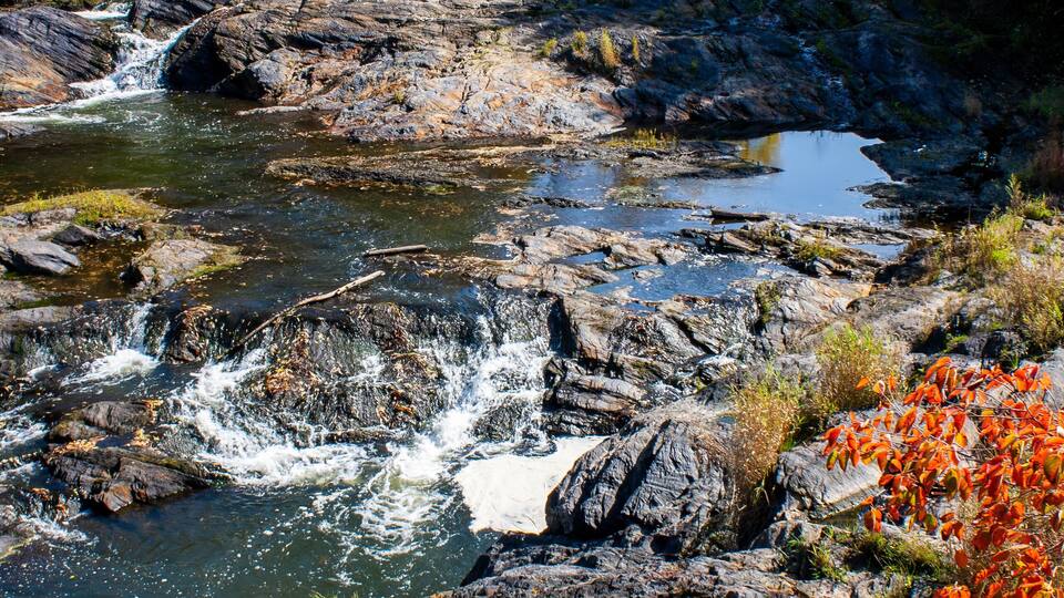 A waterfall cascading over rocks in a forested area with autumn foliage.
