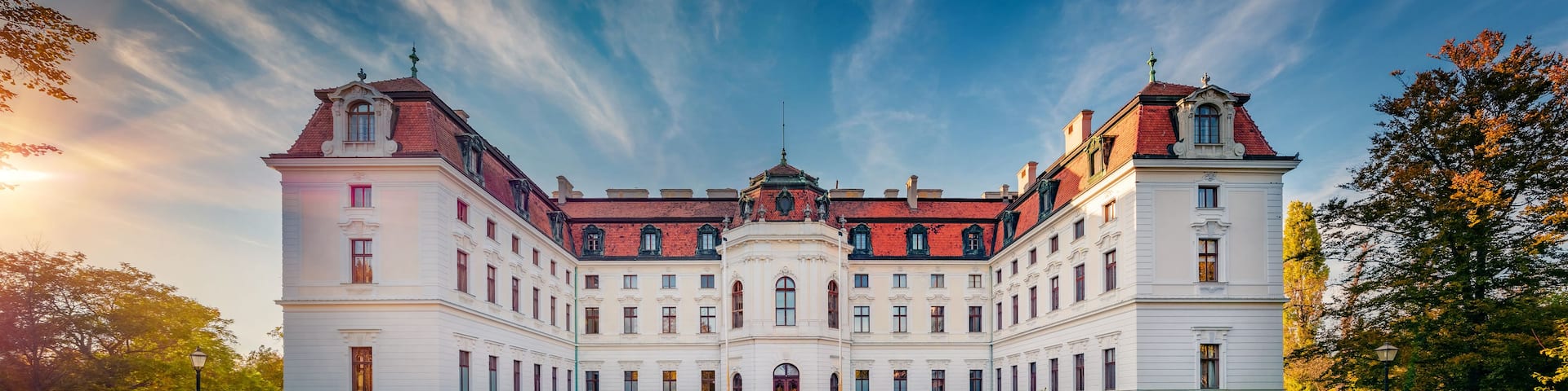 A large, ornate building with a symmetrical facade, a central tower, and a cobblestone courtyard.