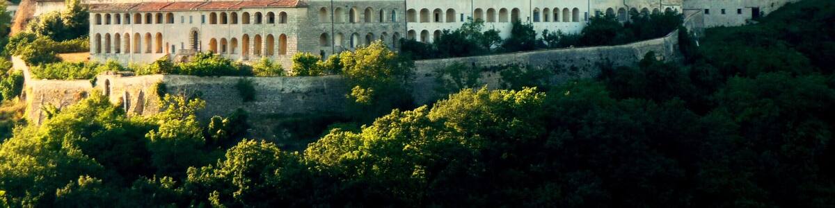 Eine historische Burg mit einem markanten Glockenturm, umgeben von üppiger Vegetation und auf einem Hügel gelegen.