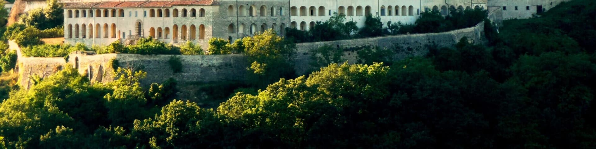 A historic castle with a prominent clock tower, surrounded by lush greenery and perched on a hillside.