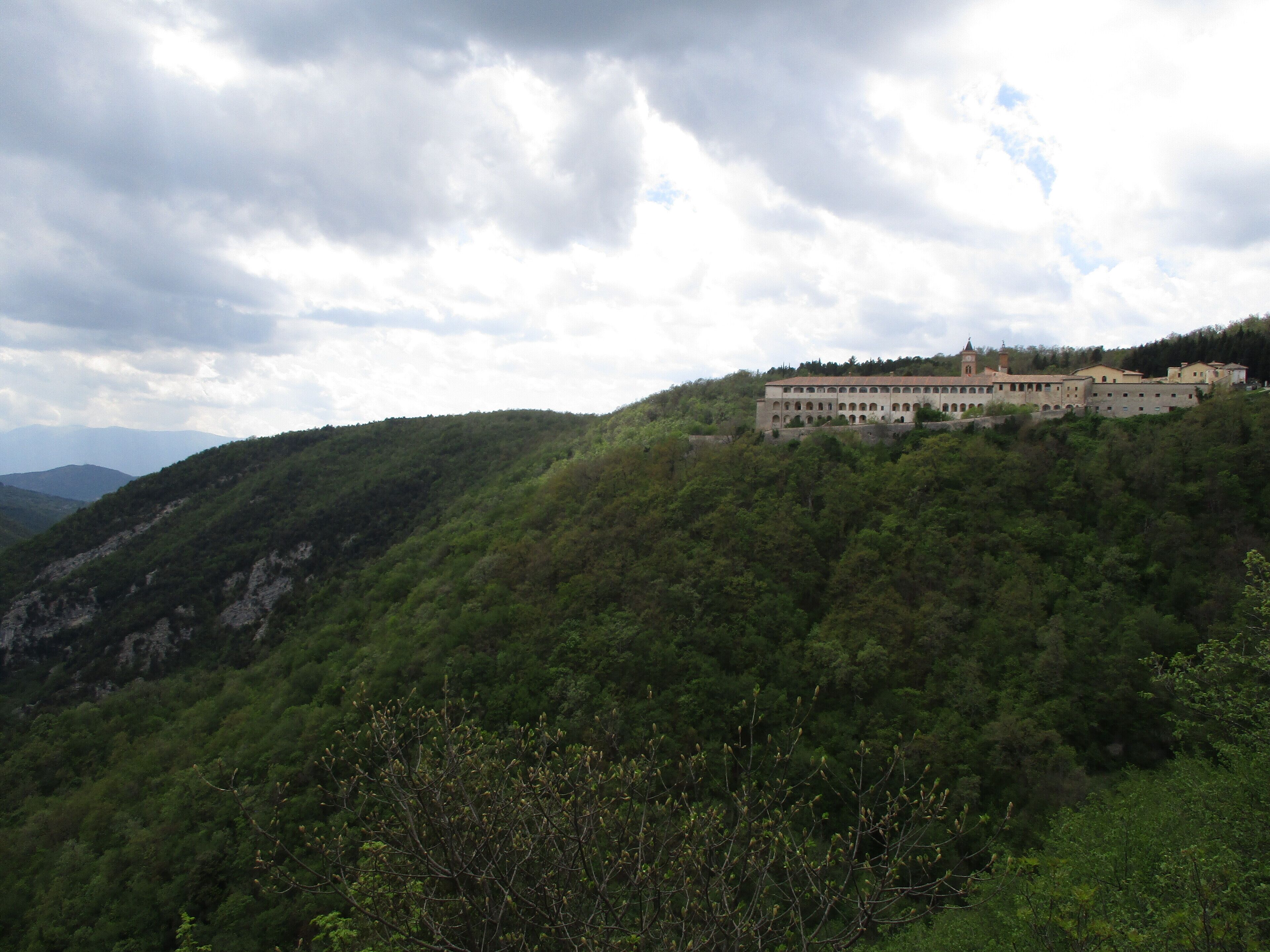 A historic building on a hillside with lush greenery and a cloudy sky.