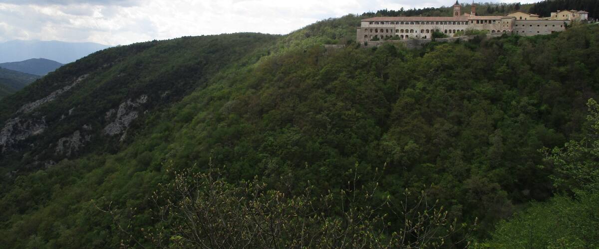 A historic building on a hillside with lush greenery and a cloudy sky.