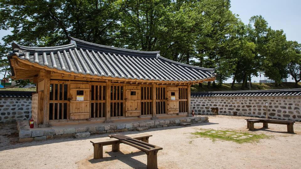 A traditional Korean pavilion with a tiled roof, wooden structure, and stone wall.