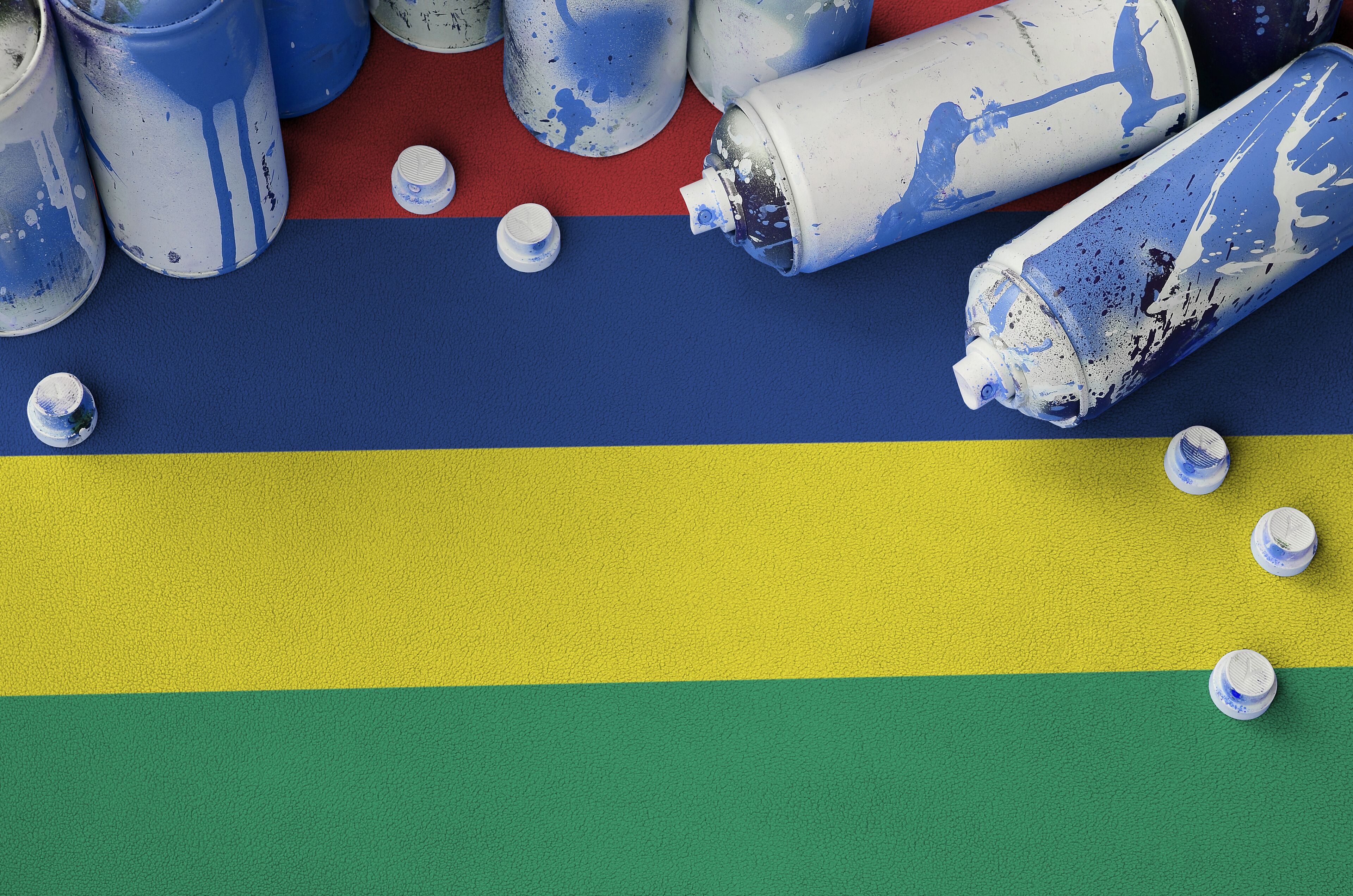 Spray paint cans and caps on a surface with horizontal stripes of blue, yellow, and green.