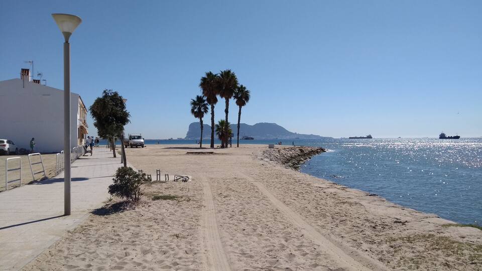 A sandy beach with palm trees, a white building, and a clear blue sky.