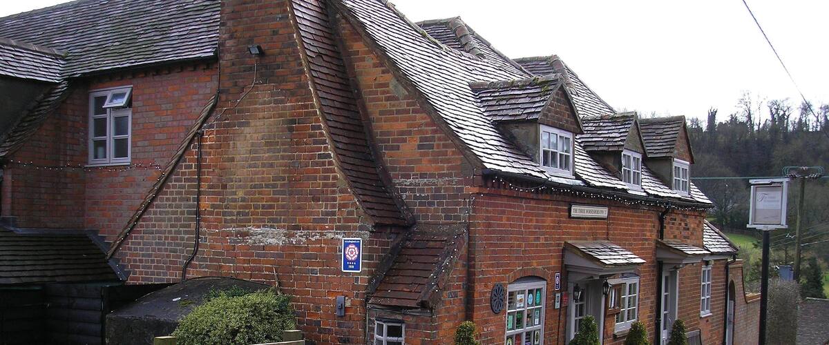 A traditional brick building with a sloped roof, a wooden fence, and potted plants.