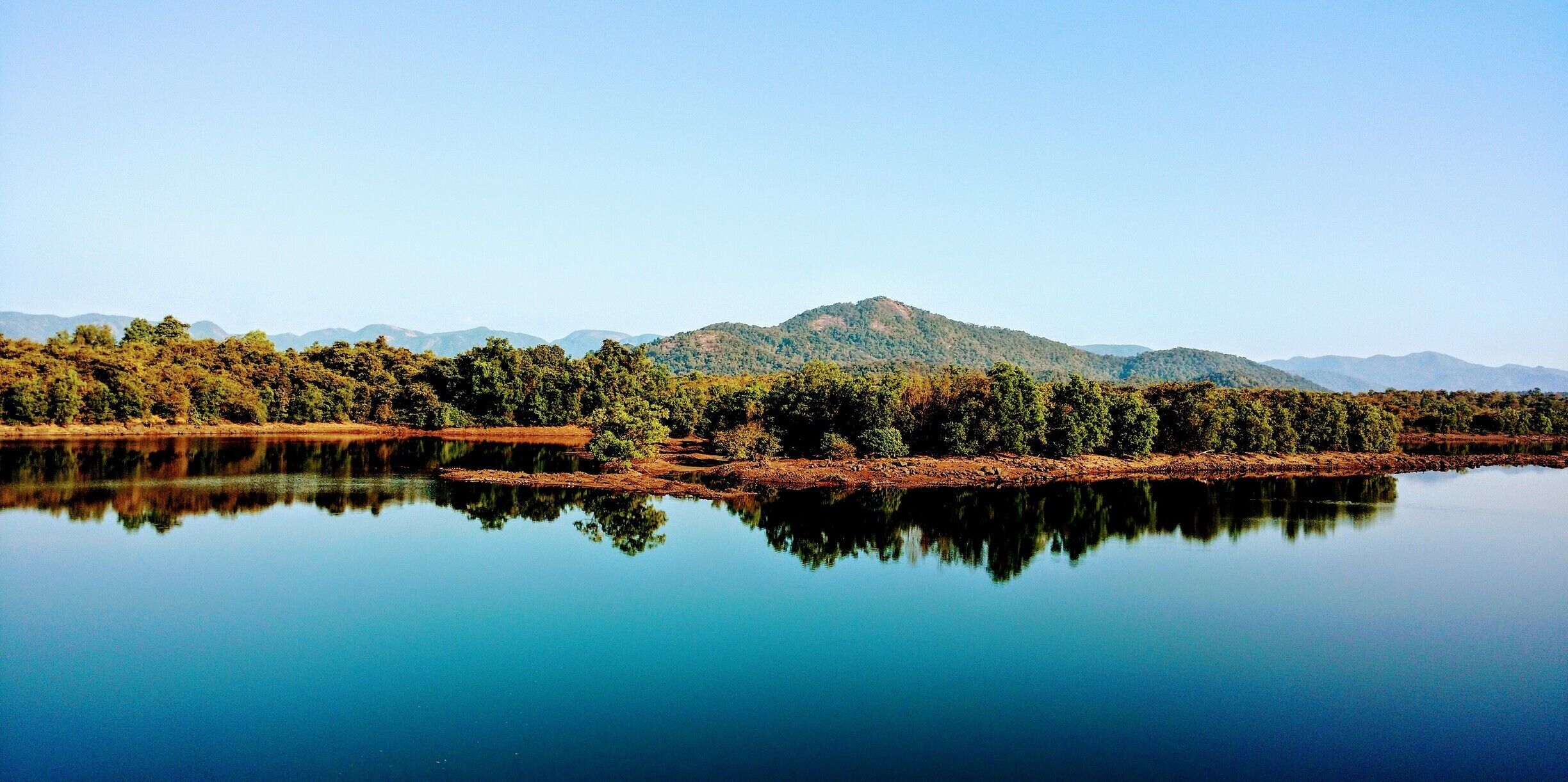 A calm lake reflecting trees and mountains.