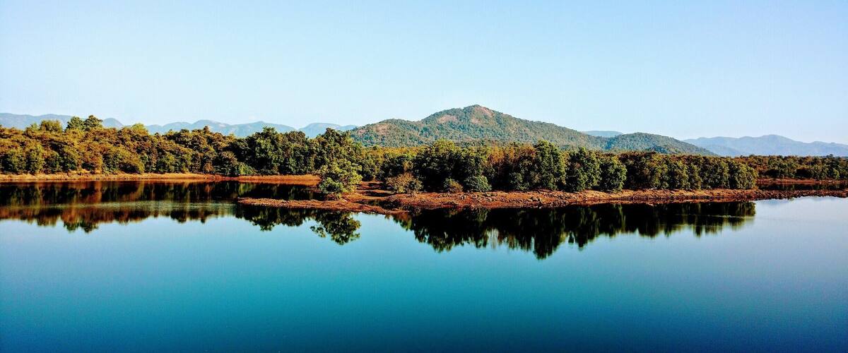 A calm lake reflecting trees and mountains.