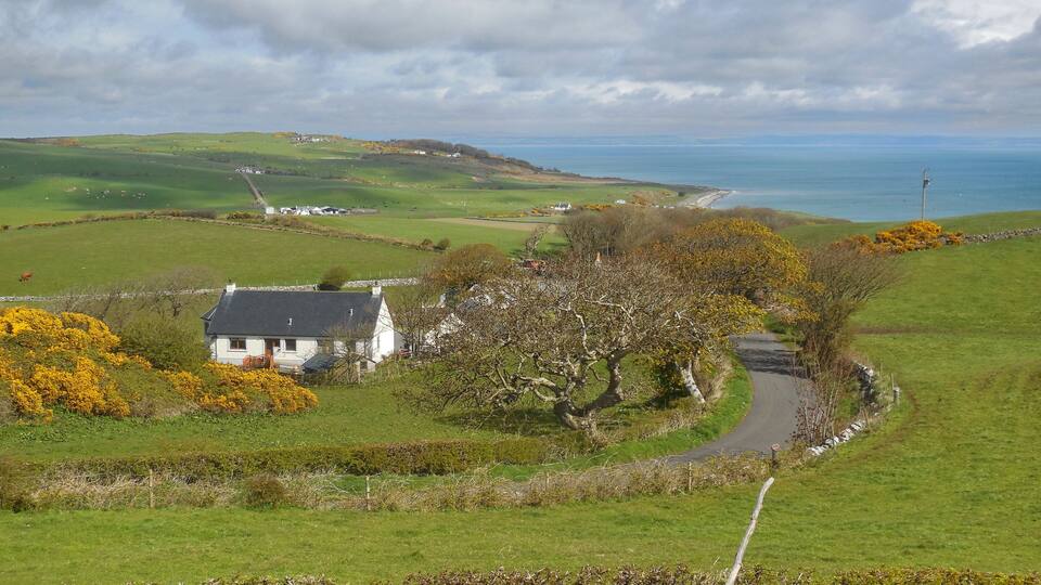 A coastal landscape with rolling hills, a white house, and a winding road.