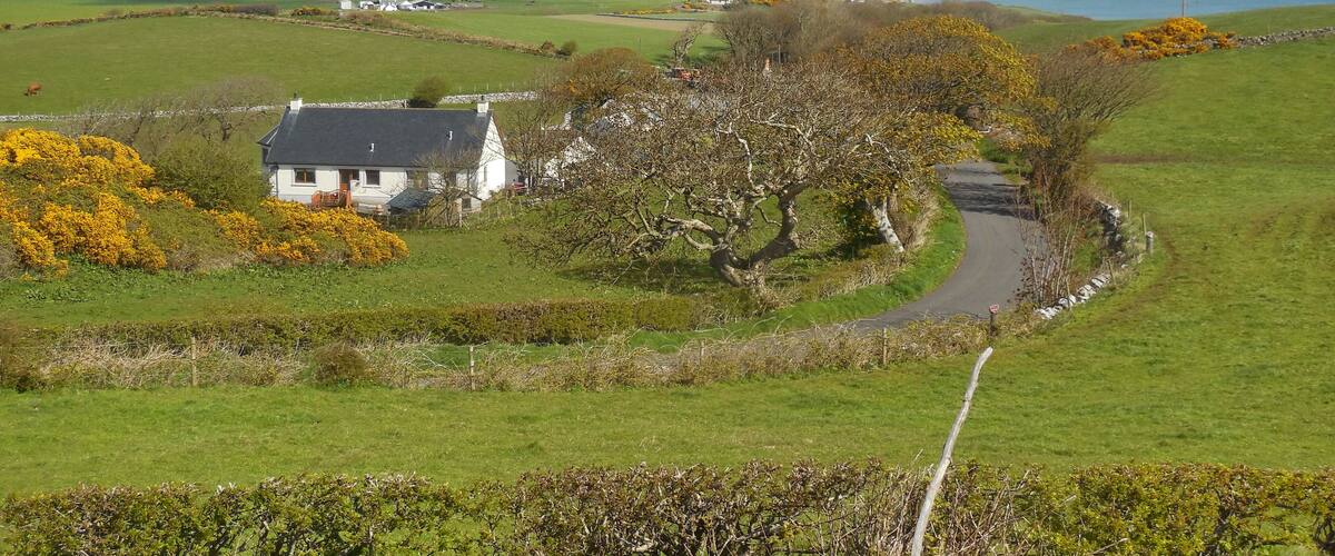 A coastal landscape with rolling hills, a white house, and a winding road.