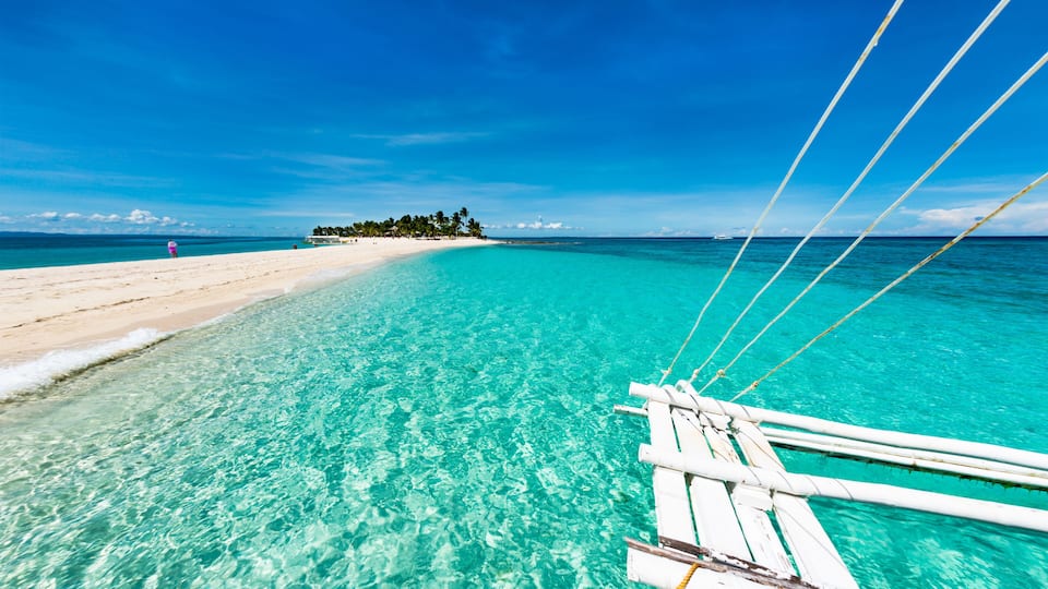 A clear turquoise sea, a sandy beach, and a small island with trees in the distance.
