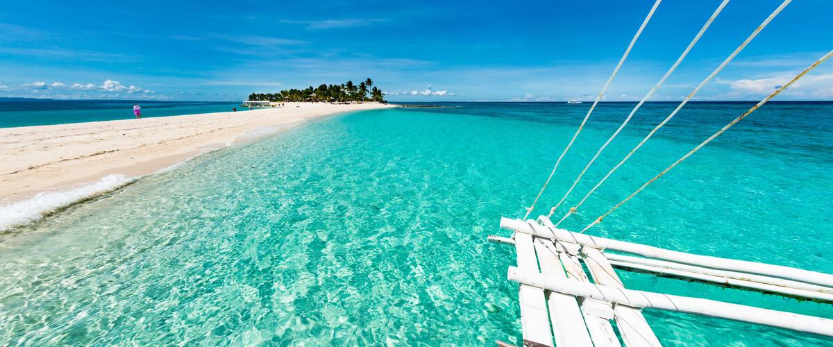 A clear turquoise sea, a sandy beach, and a small island with trees in the distance.