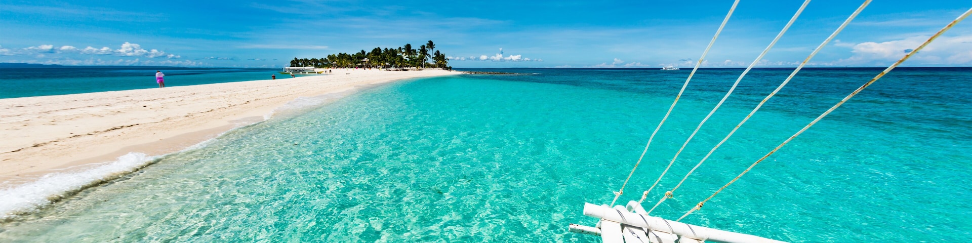 A clear turquoise sea, a sandy beach, and a small island with trees in the distance.