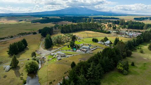 High-angle view of a rural farm, featuring buildings, pastures, and a mountain backdrop. Tranquil countryside scene. WAIOURU, MANAWATU-WANGANUI, NEW ZEALAND