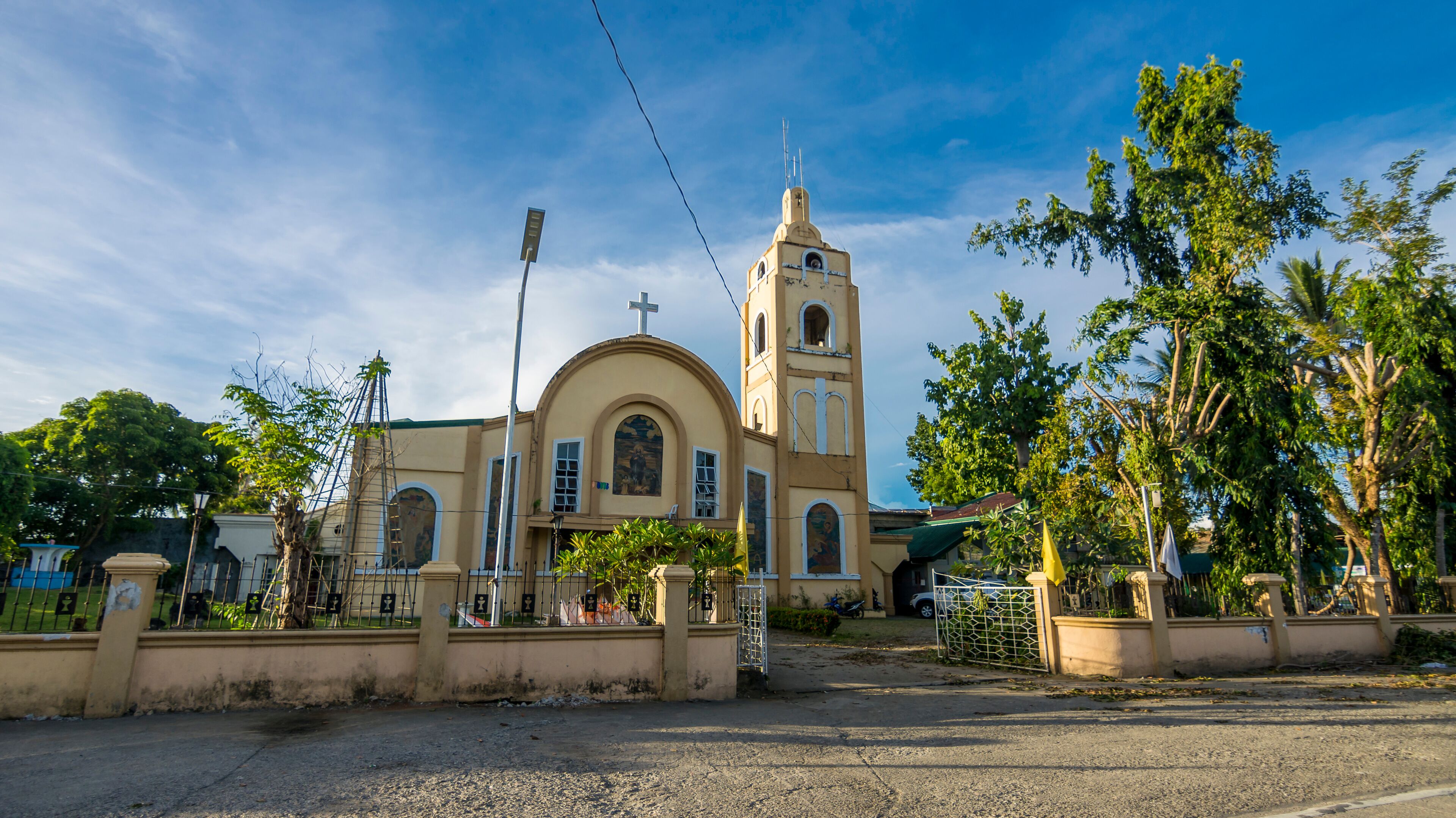 A church with a bell tower and a cross on top, surrounded by trees and a fence.