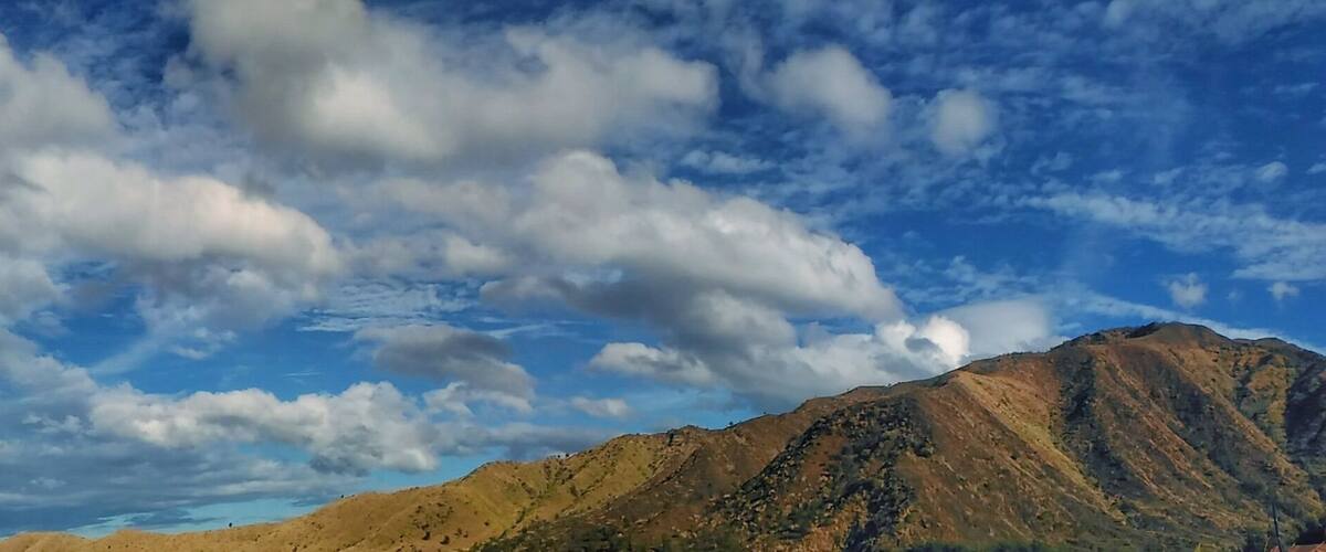 A mountain with a clear sky and scattered clouds.