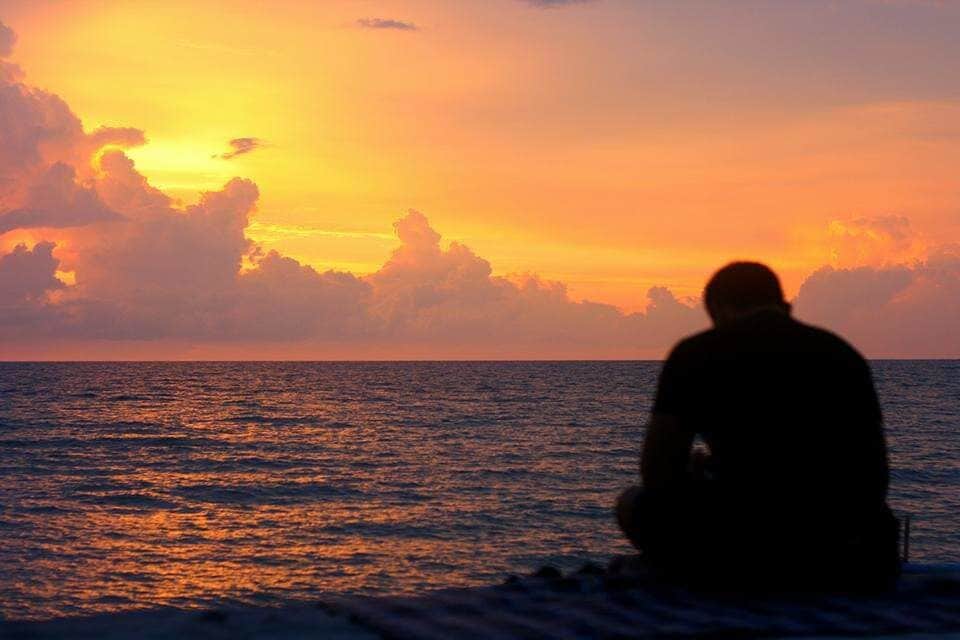 A silhouette of a person sitting on the beach during sunset.