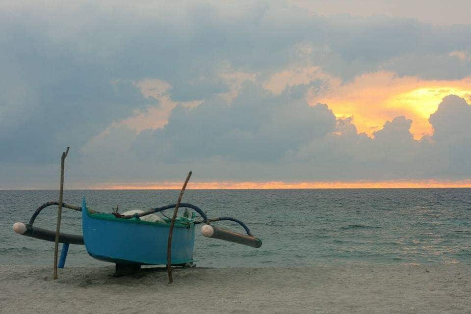 A blue boat on a sandy beach with a sunset in the background.