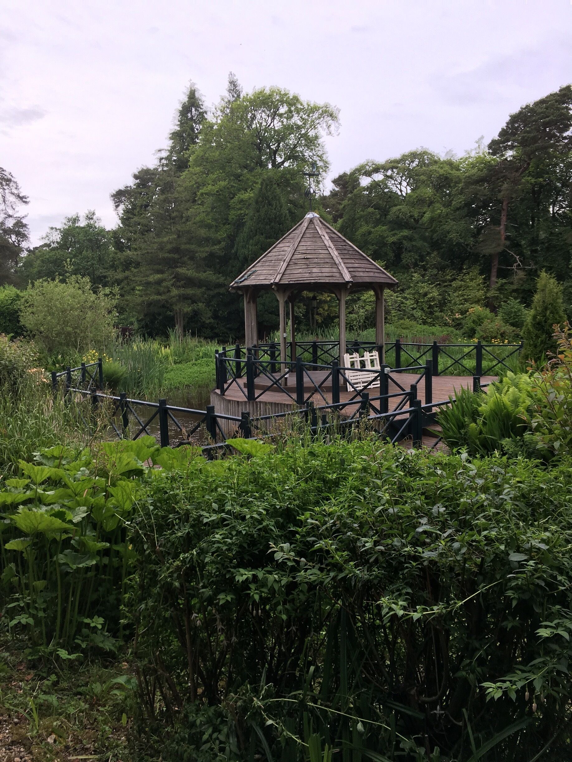 A wooden gazebo surrounded by lush greenery and a wooden fence.