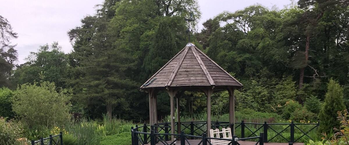 A wooden gazebo surrounded by lush greenery and a wooden fence.
