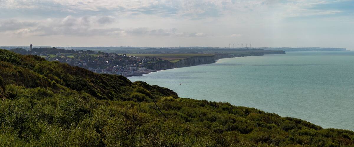 A coastal landscape with a cliff, a town, and wind turbines in the distance.