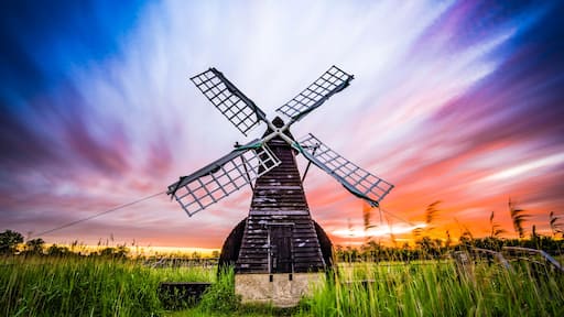 A windmill with four sails in a field during sunset.