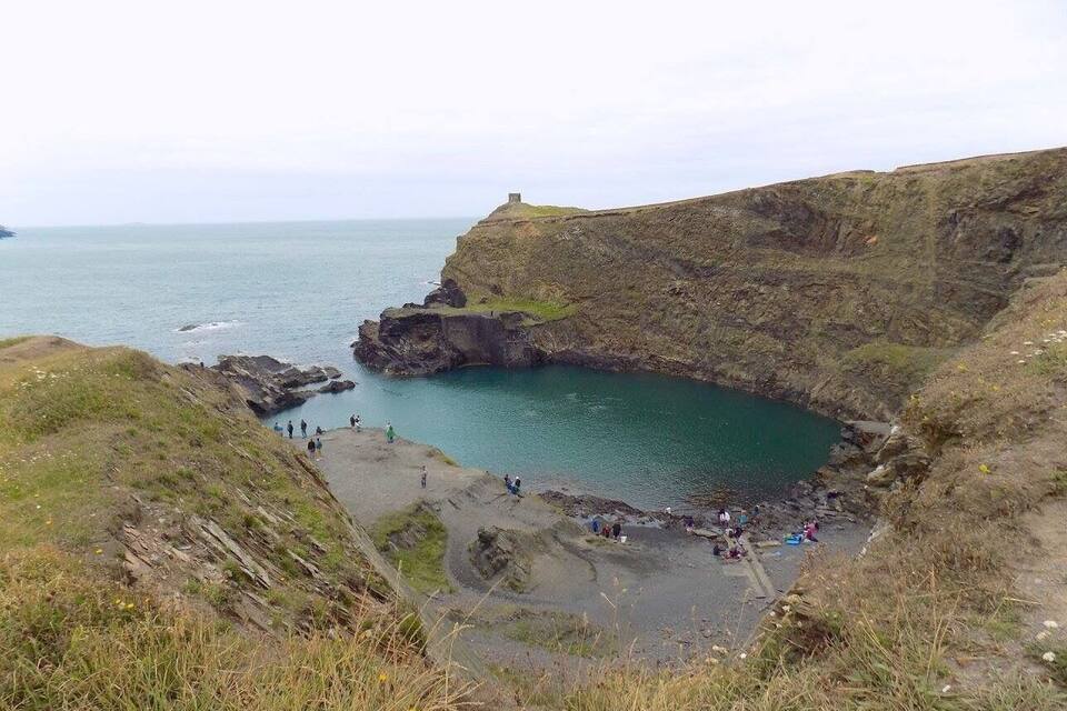 A coastal landscape with a rocky cliff, a small cove, and a distant view of the sea.