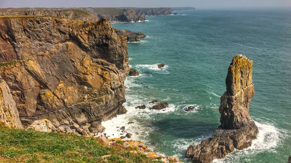 A coastal cliff with a prominent rock formation and waves crashing against it.