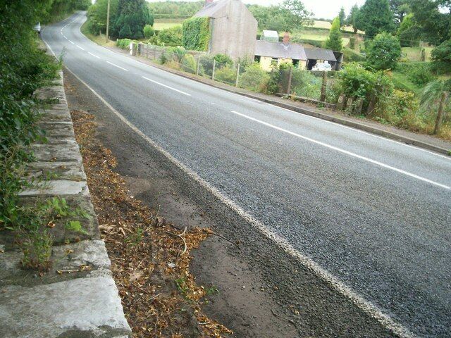 A rural road with a stone wall on the left and a large, cylindrical structure in the distance.