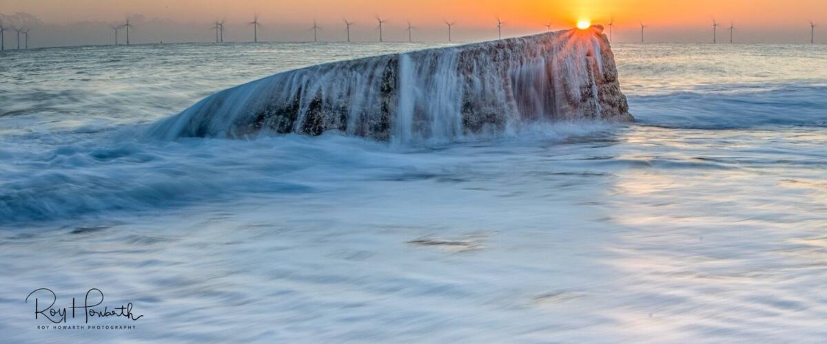 A waterfall in the ocean with the sun setting in the background.