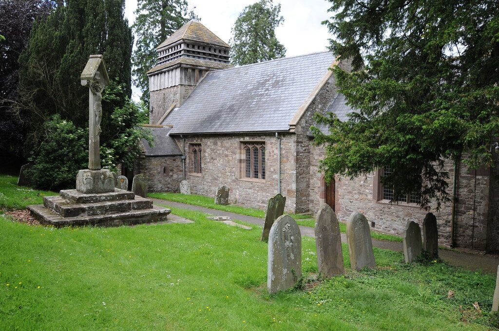 A church with a stone structure, a graveyard with headstones, and a tall tree in the foreground.