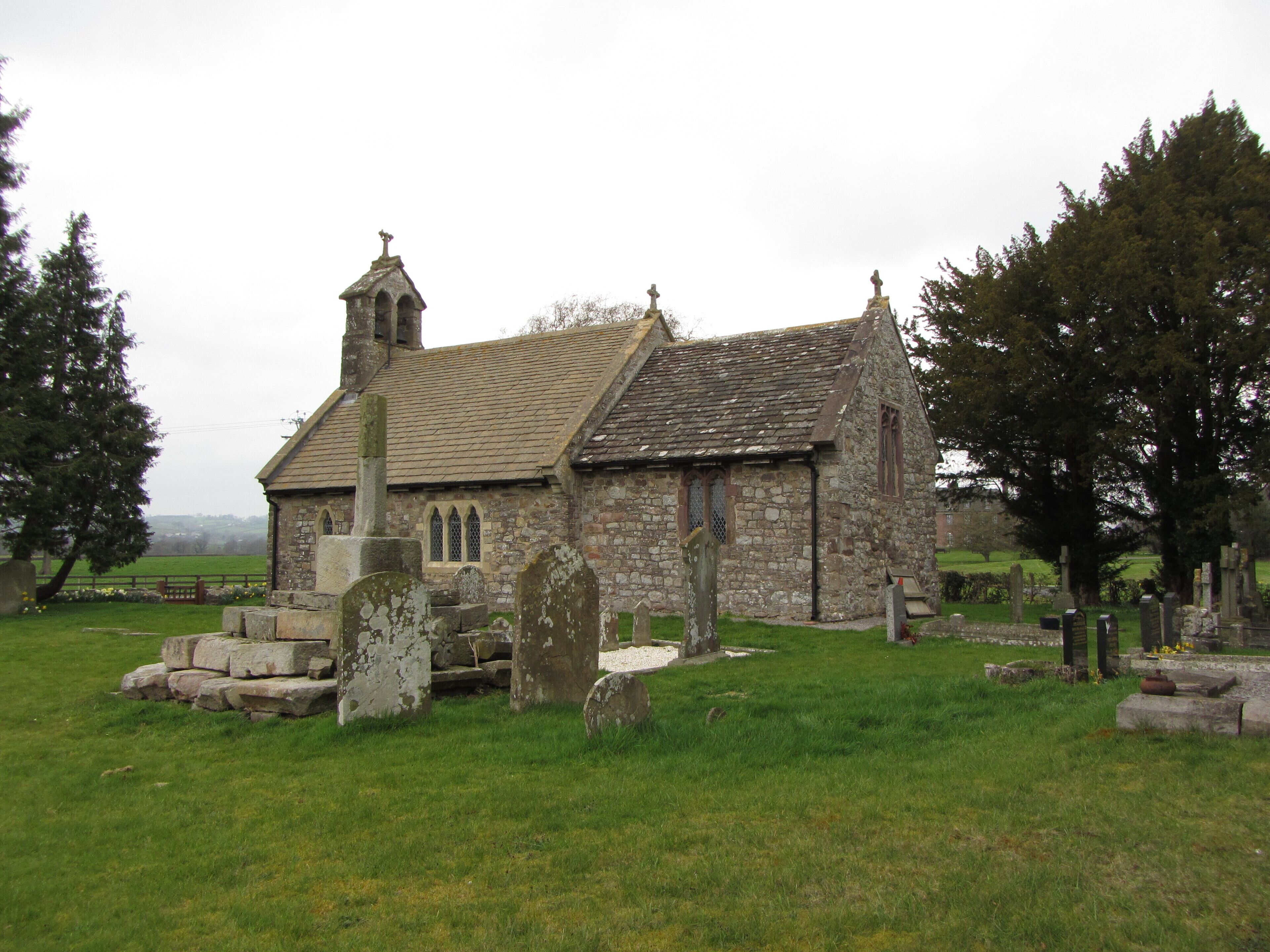 A small stone church with a bell tower and a graveyard in front.