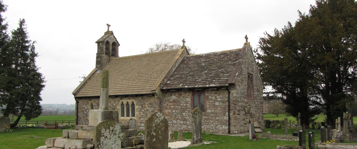 A small stone church with a bell tower and a graveyard in front.