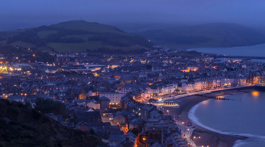 A coastal town at dusk with illuminated buildings and a curved bay.