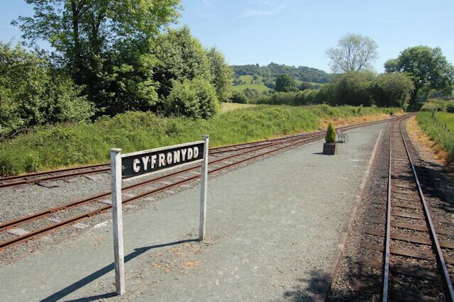 A railway track with a sign reading "CYFRONYDD" and a small potted plant on the platform.