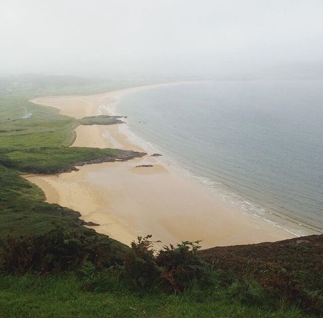 A coastal landscape with a sandy beach, grassy areas, and a calm sea.