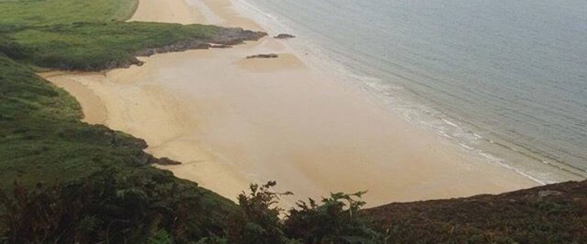 A coastal landscape with a sandy beach, grassy areas, and a calm sea.