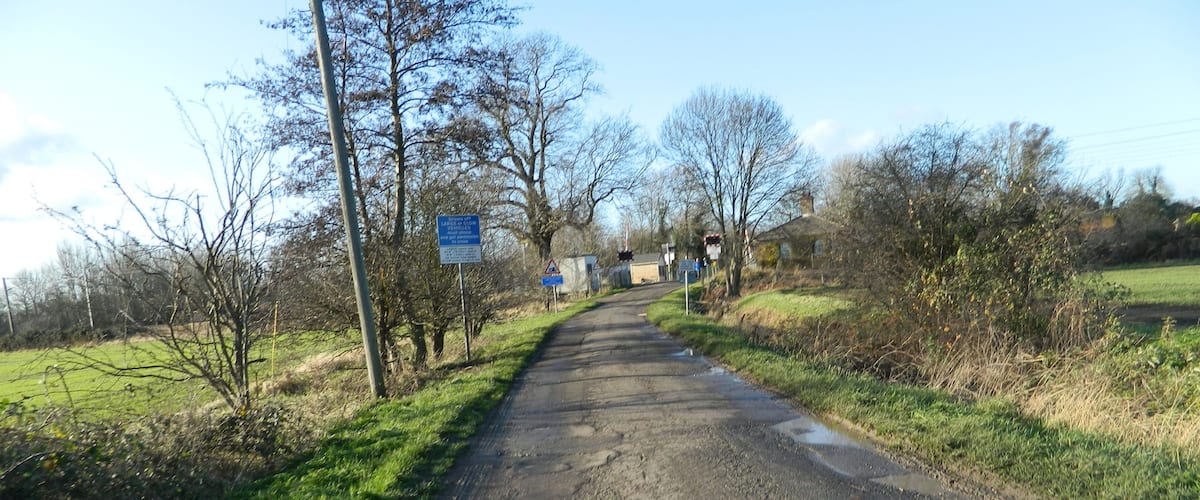 A rural road with a blue sign on the left, surrounded by trees and grass.