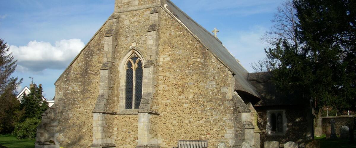 A stone church with a bell tower, a large arched window, and a grassy cemetery with headstones.