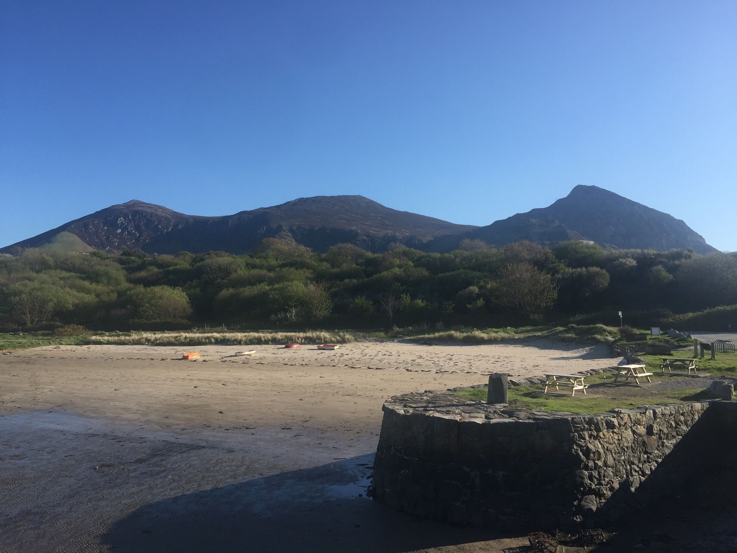 A beach with a stone structure, a river, and mountains in the background.