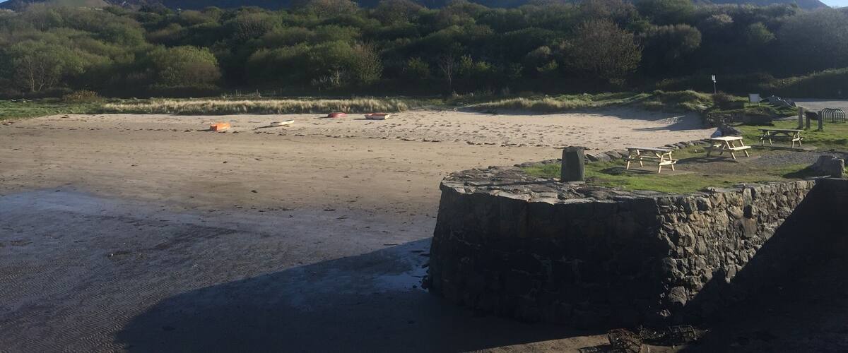 A beach with a stone structure, a river, and mountains in the background.