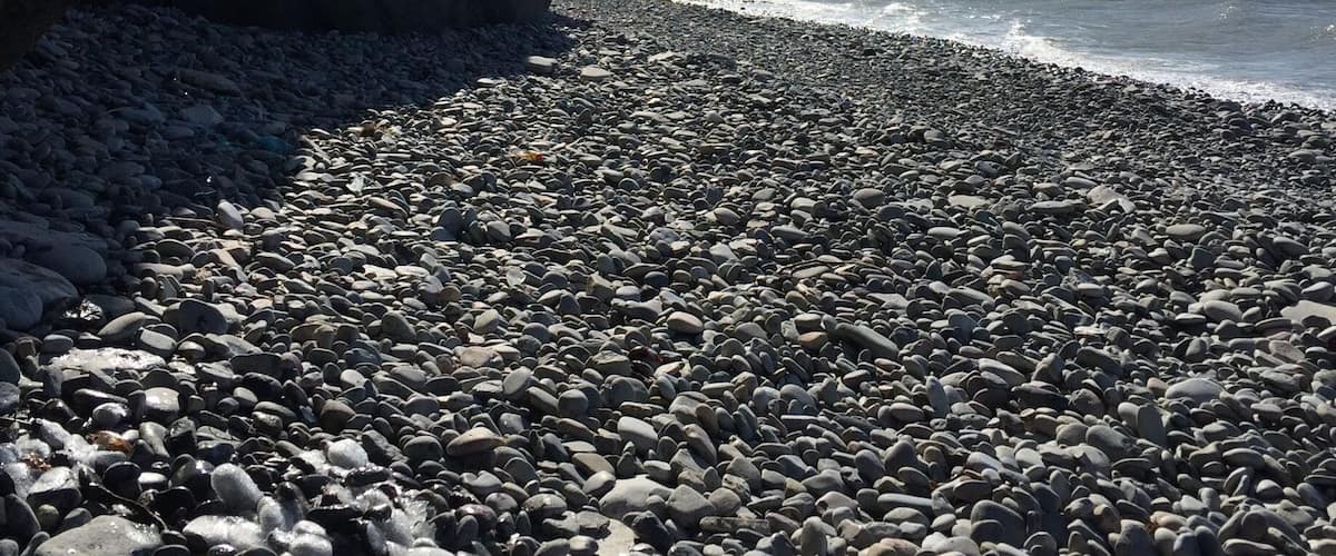 Uma praia rochosa com formações de gelo e um céu claro.
