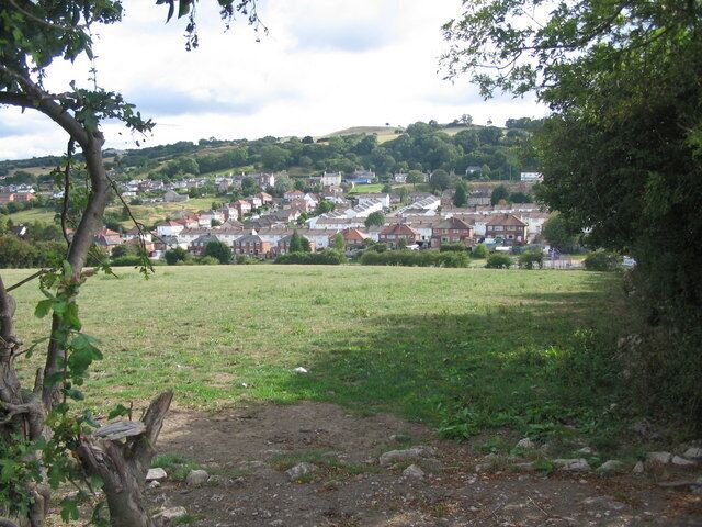 A rural landscape with a field, trees, and a village in the distance.